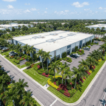 Coastal South Florida commercial landscape with shrubs and small trees showing brown, salt-scorched leaf edges and one-sided damage facing the ocean, alongside healthy salt-tolerant plants near a modern coastal office building.